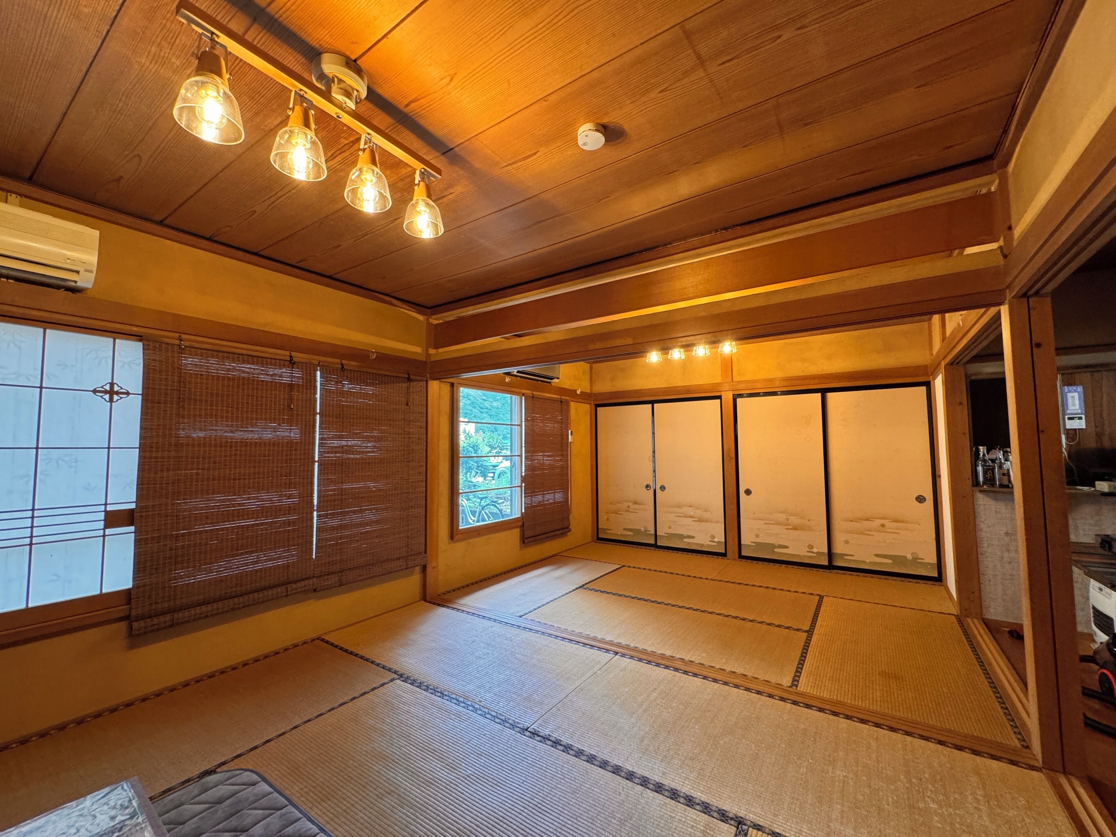 Una habitación japonesa tradicional con suelo de tatami, puertas correderas e iluminación colgante en el techo.