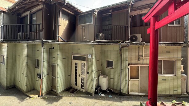 A traditional Japanese building with a tiled exterior, a red torii gate, and a small utility shed.