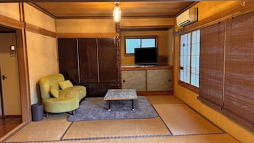 A traditional Japanese room with tatami flooring, a sofa, a television, and a sliding door.