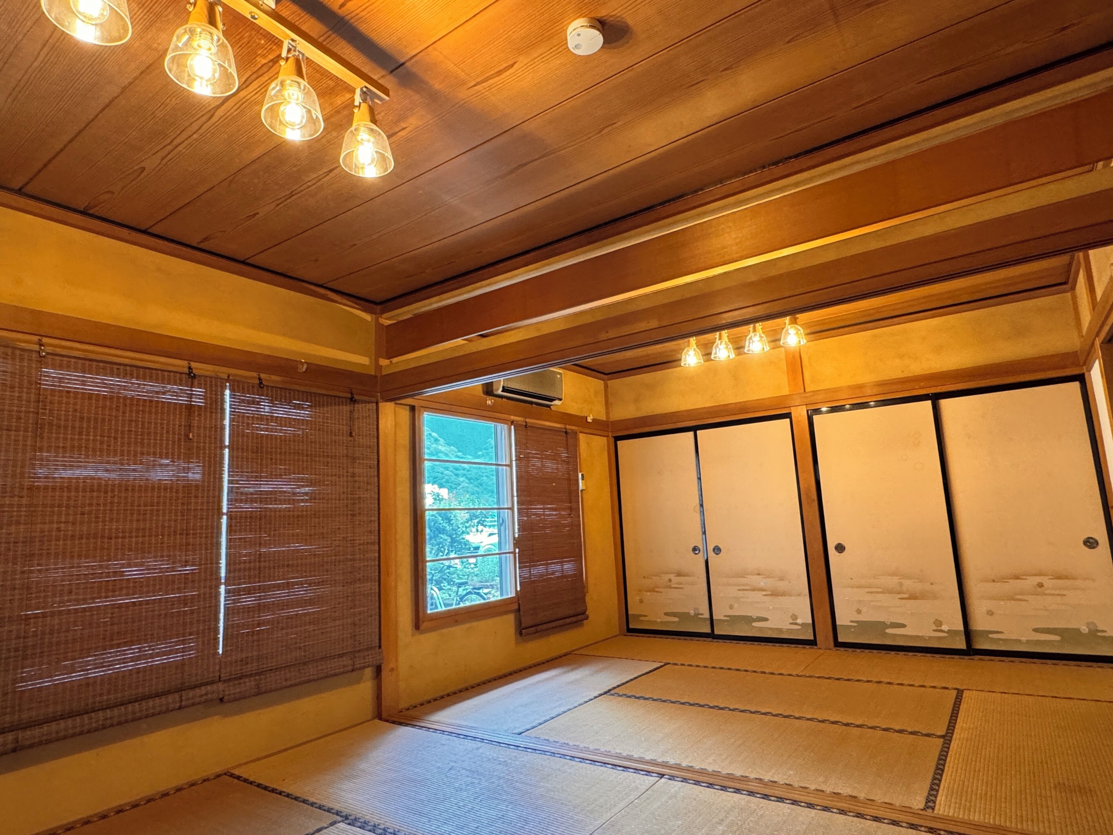Una habitación japonesa tradicional con suelo de tatami, puertas correderas y un techo con lámparas colgantes.