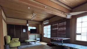 A traditional Japanese room with tatami flooring, a green sofa, a television, and a sliding door. - Calmbase Nishiizu Izayoi (Numazu)