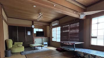 A traditional Japanese room with tatami flooring, a green sofa, a television, and a sliding door.