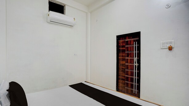 A room with a bed, a window with a metal grille, an air conditioning unit, and a wall socket. - Hotel O Prayagraj Sangam Railway (Prayagraj)