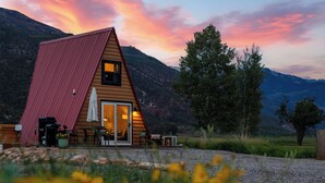Eine Hütte mit geneigtem Dach, einer Terrasse mit Sitzgelegenheit und Blick auf die Berge.