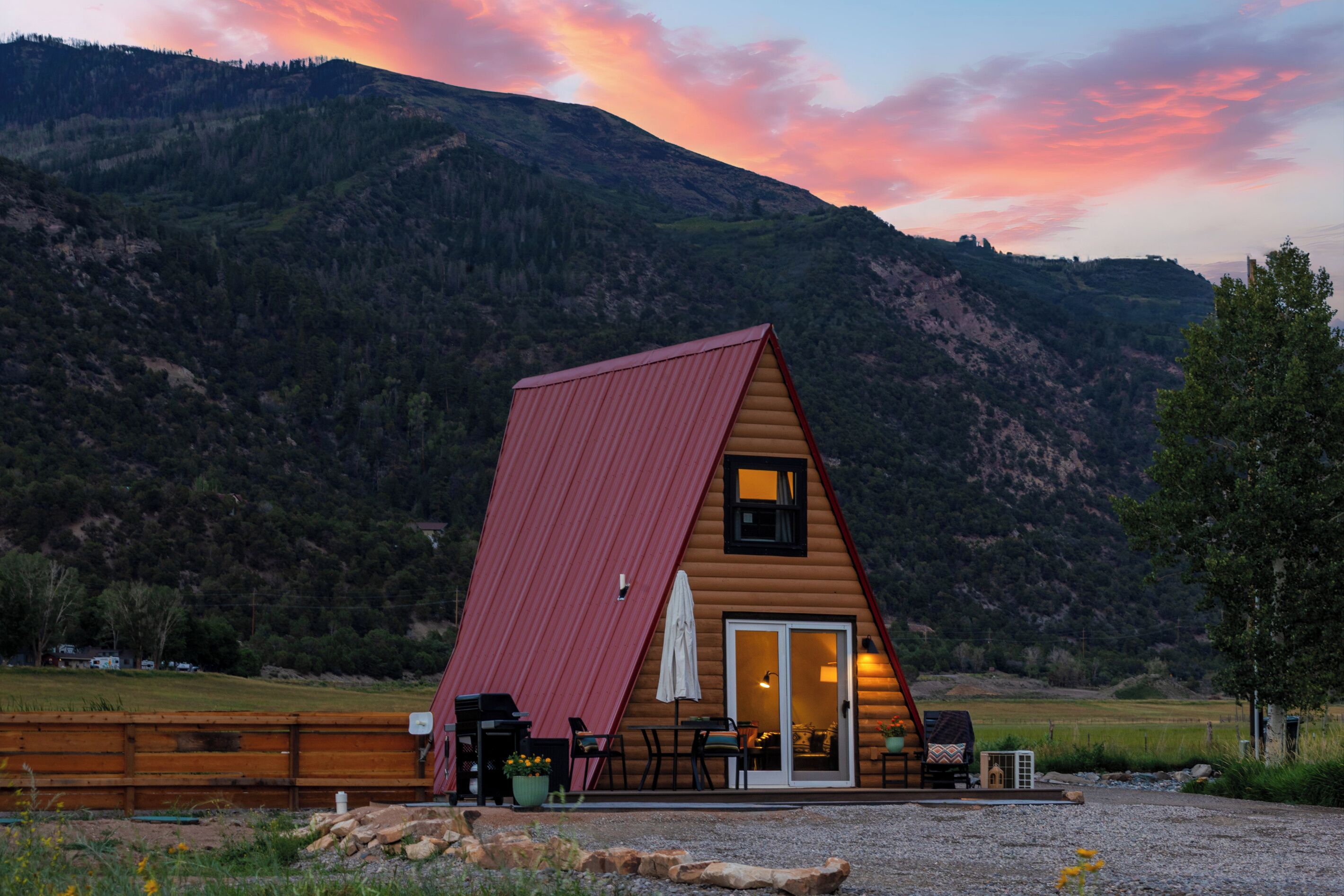 A wooden cabin with a red roof, a patio with outdoor furniture, and a view of a mountainous landscape.