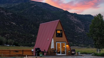 A wooden cabin with a red roof, a patio with outdoor furniture, and a view of a mountainous landscape.