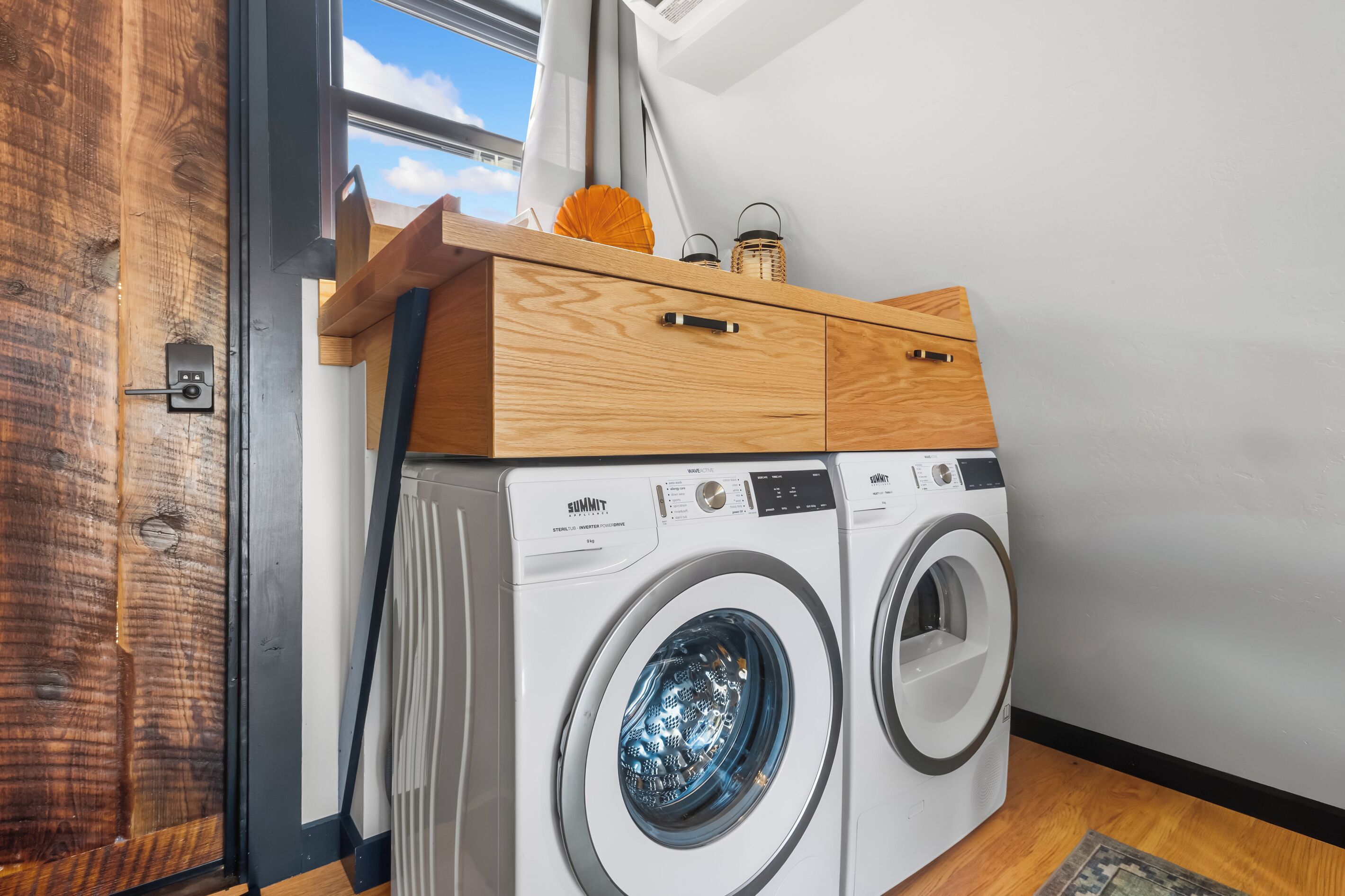 A laundry room with two front-loading washing machines, a wooden cabinet, and a window with a view of the sky.