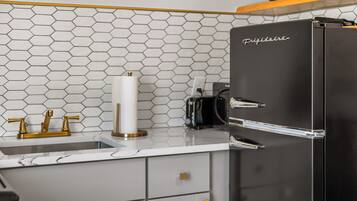 A kitchen with a black refrigerator, a sink with gold faucets, and a hexagonal tile backsplash.
