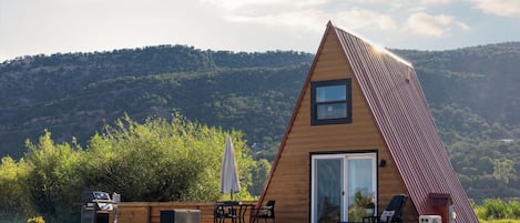 Une maison moderne en forme de triangle, construite en bois, dotée d’une grande porte-fenêtre coulissante, d’un espace salon extérieur et d’une allée en gravier.