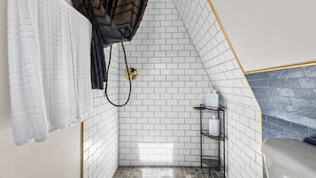 A bathroom with white tiled walls, a shower area, and a black metal shelf with toiletries.
