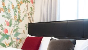Een bed met een zwart hoofdeinde, wit beddengoed en drie kussens in rood, grijs en wit.