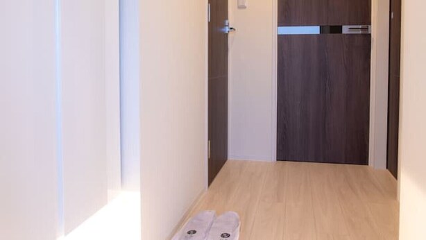 Un pasillo con una puerta de madera, un interruptor de luz y un par de zapatos en el suelo.