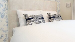 Une chambre à coucher avec un lit, un papier peint à motifs floraux et deux oreillers portant le nom d’une marque.