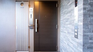 L’entrée d’un hôtel, avec une porte à deux battants, un écran numérique indiquant l’étage de l’ascenseur et un mur à texture.