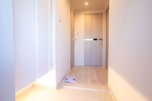 Ein schmaler Flur mit einer Holztür am Ende, gefliestem Boden und einem Teilblick auf eine weiße Wand.