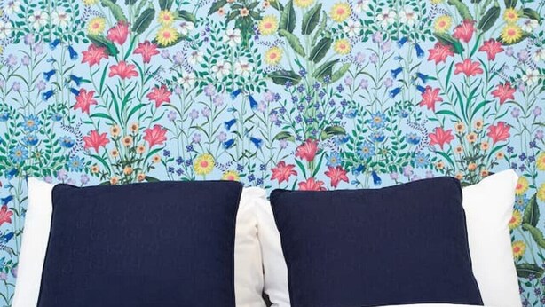 En säng med mörkblå kuddar och en sänggavel med blommönster.