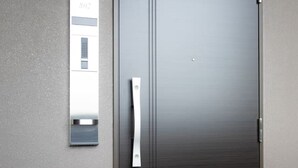 En mörkfärgad dörr med ett metallhandtag och en liten rektangulär spegel som sitter fast på väggen till vänster om dörren.