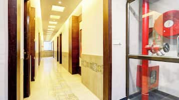 A hotel corridor with a tiled floor, wooden doors, and a glass wall displaying a red fire extinguisher.