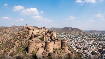 A historic fort with multiple towers and walls, surrounded by a town and hills.
