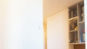 Un pasillo con piso de madera, pared blanca y un aparador de vidrio con diversos objetos.
