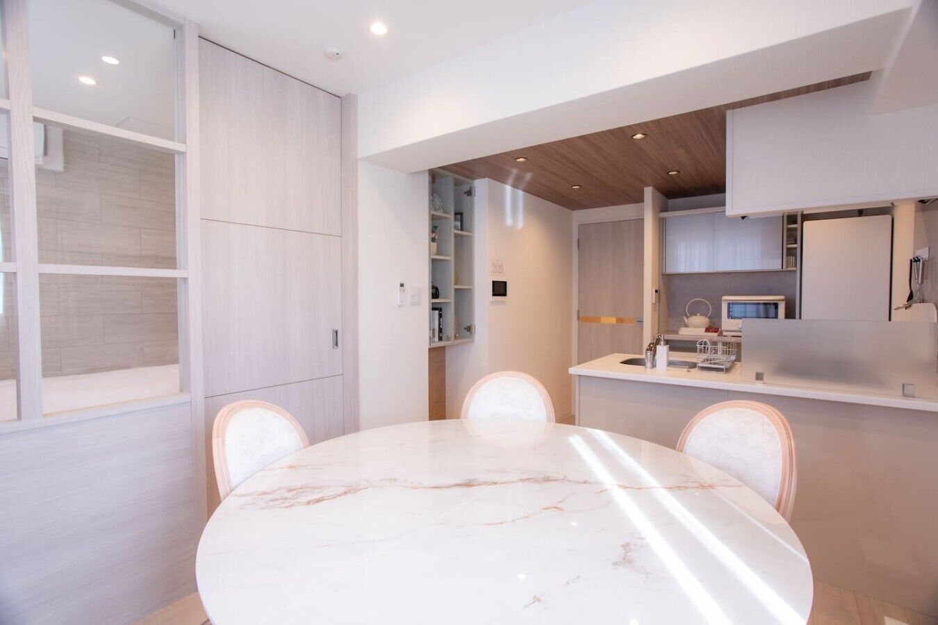 A modern kitchen with built-in appliances, a dining area with a marble table, and a white color scheme.