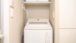 Ein kleiner Hauswirtschaftsraum mit einer Waschmaschine mit Frontlader, einem Regal mit gefalteten Handtüchern und einer fest montierten Steuerung.