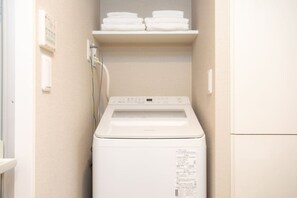 Ein kleiner Hauswirtschaftsraum mit einer Waschmaschine mit Frontlader, einem Regal mit gefalteten Handtüchern und einer fest montierten Steuerung.