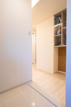 Ein Flur mit gefliestem Boden, der zu einem Raum führt, in dem ein Holzschrank Bücher und Dekoration beherbergt.