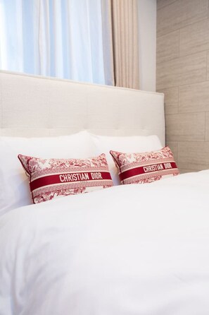 Ein Bett mit weißer Bettwäsche und zwei Kissen mit einem roten und weißen Muster sowie dem Text 'CHRISTIAN DIOR'.