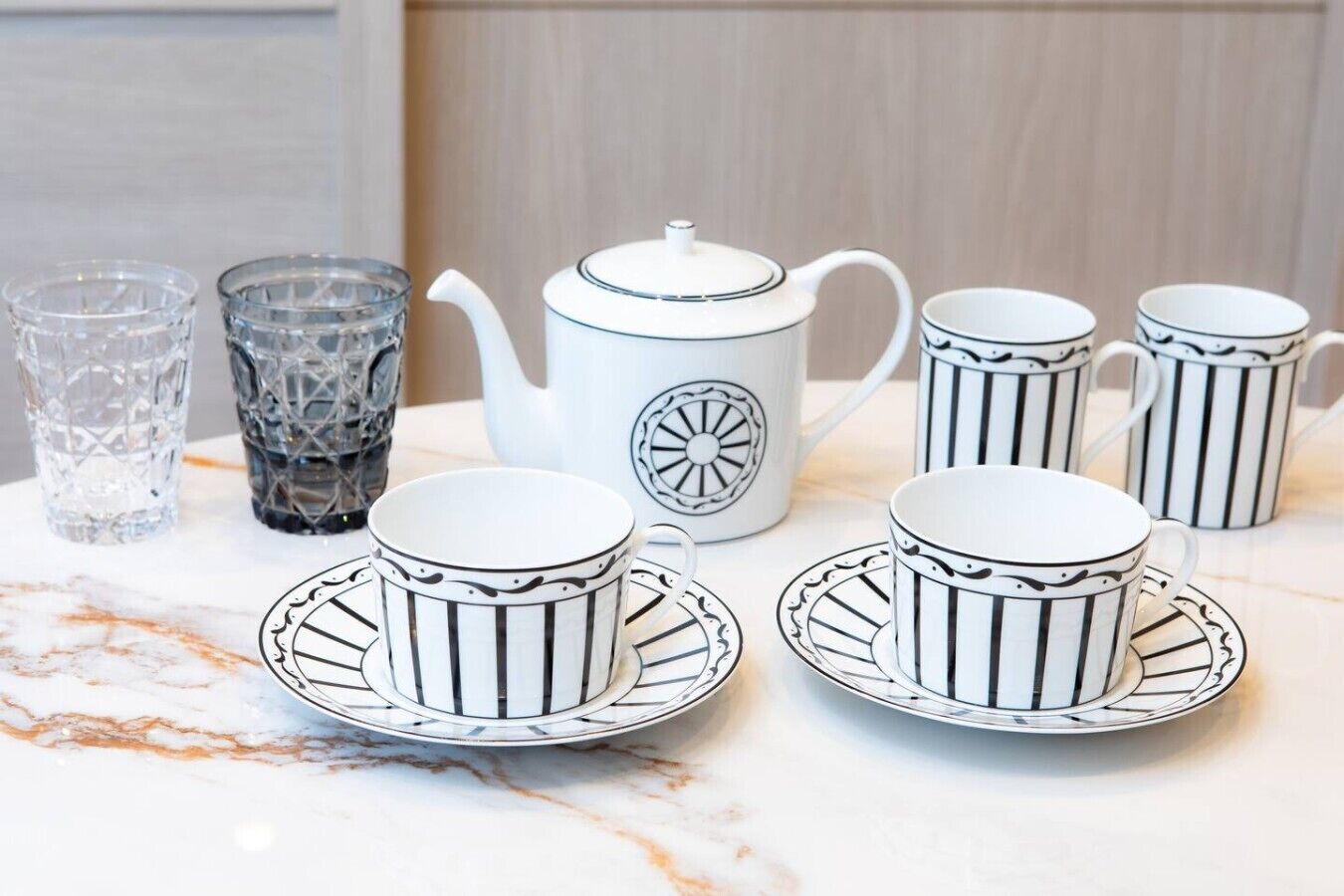 Un service à thé comprenant une théière et des tasses, posé sur une surface en marbre.