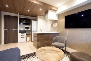 A modern living room with a round coffee table, a sofa, a TV mounted on the wall, and a kitchen area with a microwave. - 1 min walk from sta./Excellent access to central (Osaka)
