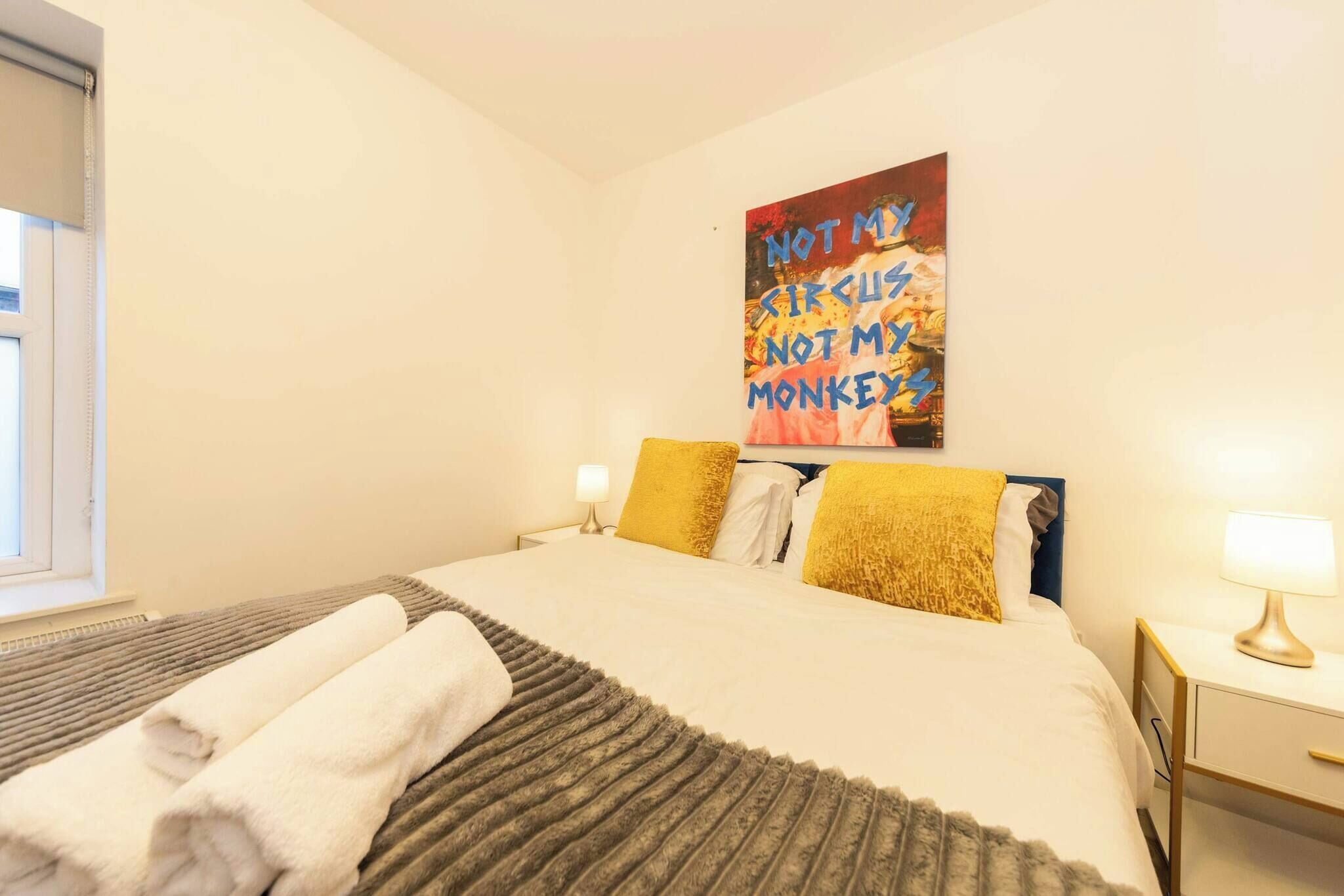 A hotel room with a bed, two bedside lamps, a window, and a wall art piece.
