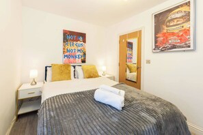 Une chambre d’hôtel avec un lit, une table de chevet, une lampe et une affiche au mur.