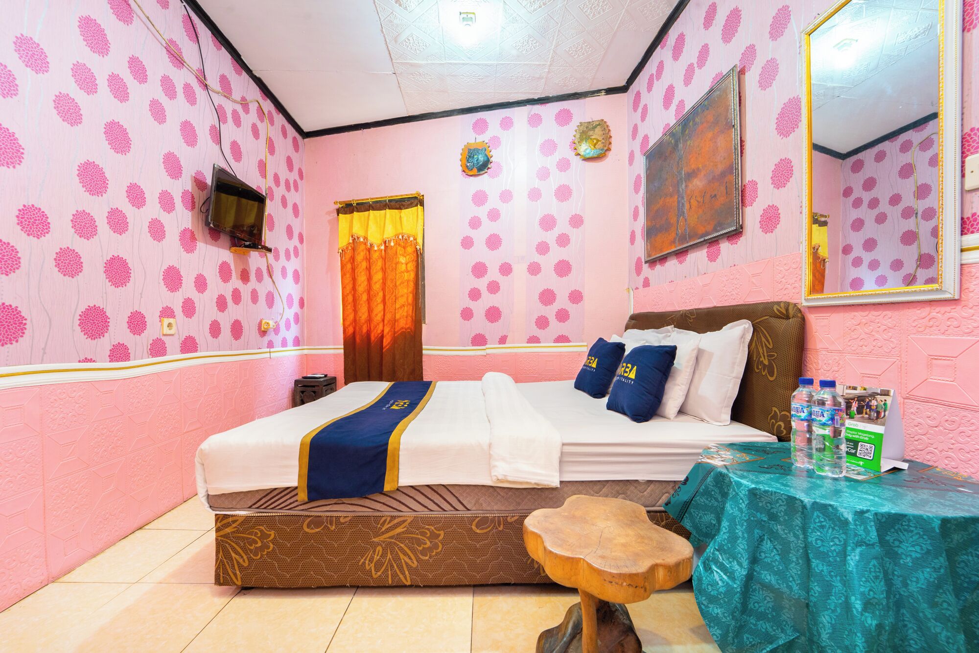 Habitación de hotel con una cama, una mesa con botellas de agua, un espejo y una ventana con cortinas.