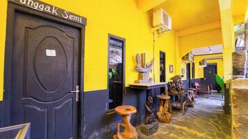 A hallway with a dark door labeled 'Jungak Semi,' a yellow wall, and various wooden sculptures.