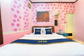 A hotel room with a bed, pillows, a painting, a mirror, and a small table with water bottles.