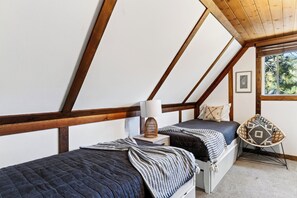 Ein Schlafzimmer mit zwei Betten, einem Fenster mit Blick auf Bäume und einer Holzbalkendecke.