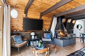 A cozy living room with a fireplace, wooden walls, and a flat-screen TV. - A-Frame | Hot Tub Deck | Fireplace | Trails, Golf & Marina | A Big Bear View (Big Bear Lake)