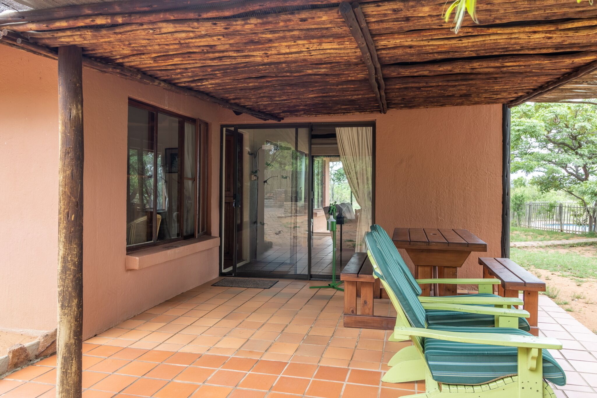Een overdekt terras met een tafel en stoelen, een deur naar een binnenruimte, en uitzicht op de omgeving.