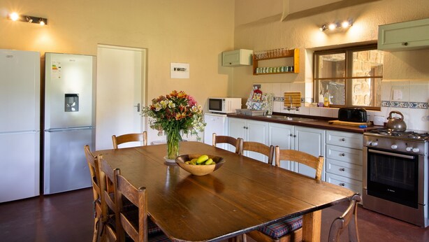 Una cocina con una mesa de comedor de madera, sillas, un refrigerador, un microondas, una estufa y un florero.