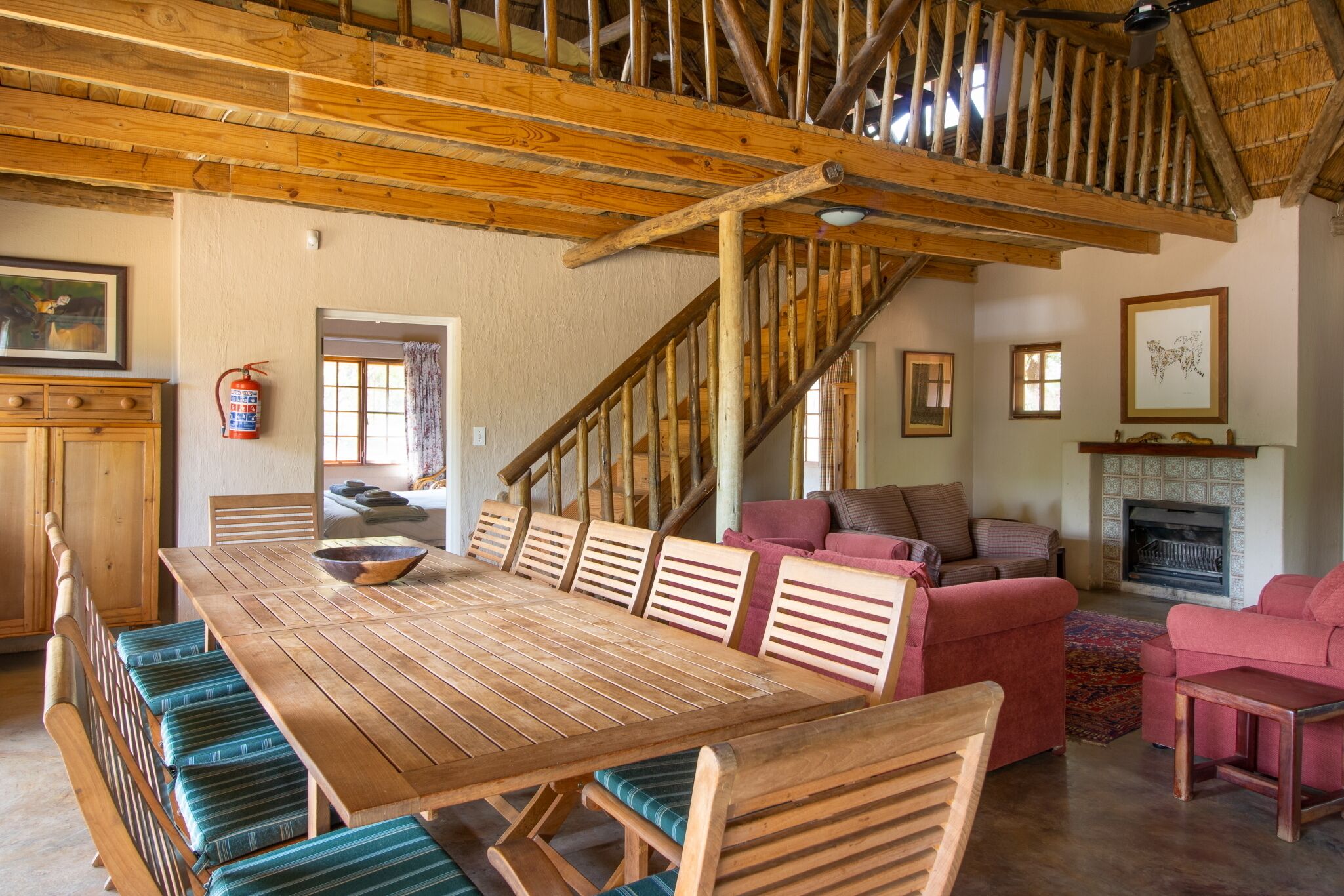 Un intérieur rustique avec une table à manger en bois, des bancs, un escalier et une cheminée.