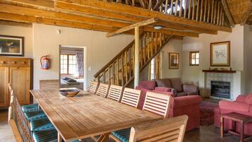 Un intérieur rustique avec une table à manger en bois, des bancs, un escalier et une cheminée.