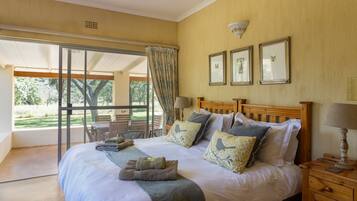 A bedroom with a large bed, a wooden headboard, and a view of a garden through a sliding glass door.