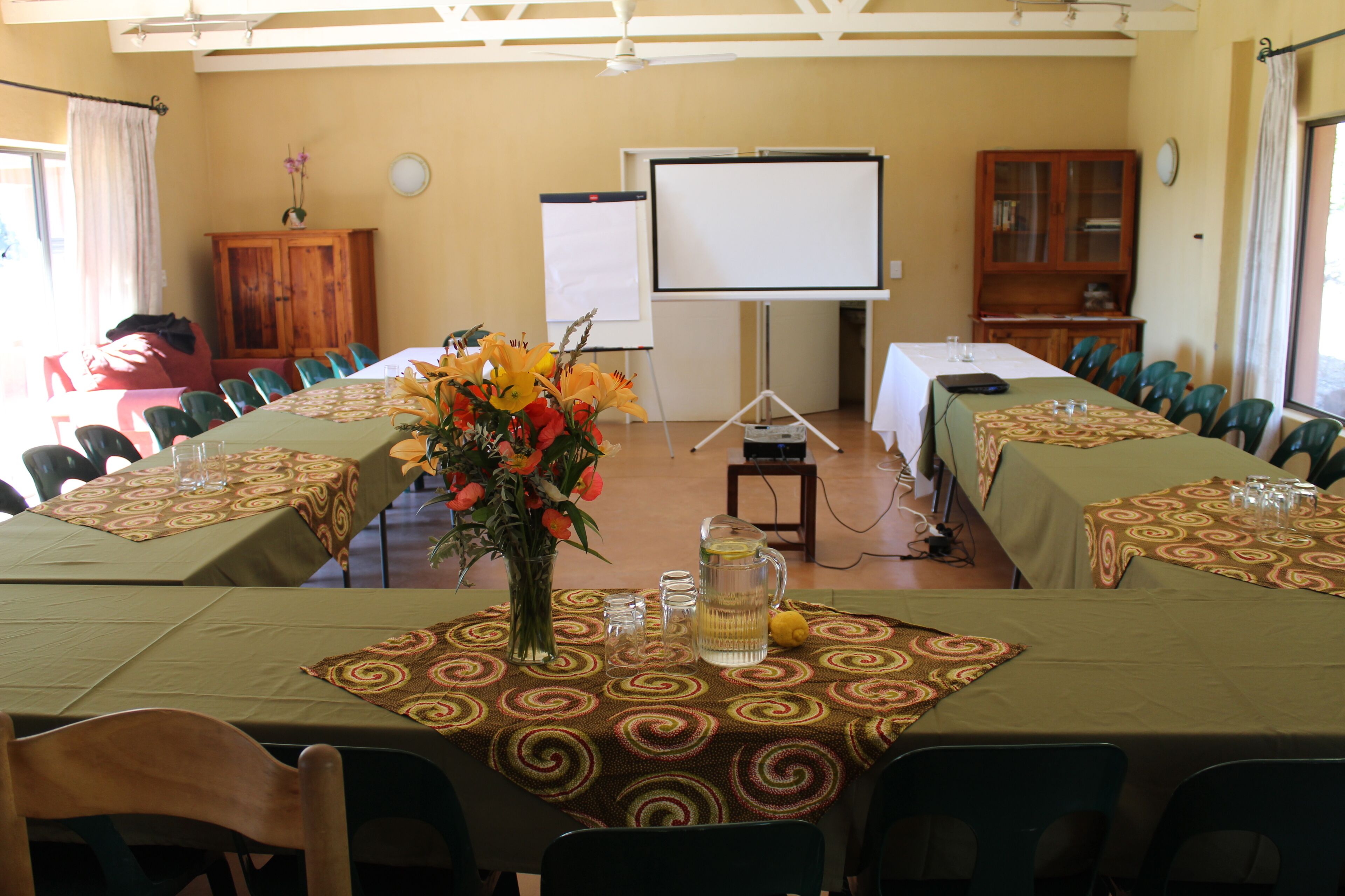 A conference room with a long table, chairs, a projector screen, and a floral centerpiece.