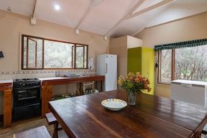 Una cocina con una mesa de madera, un refrigerador y una ventana que da a un paisaje de árboles.