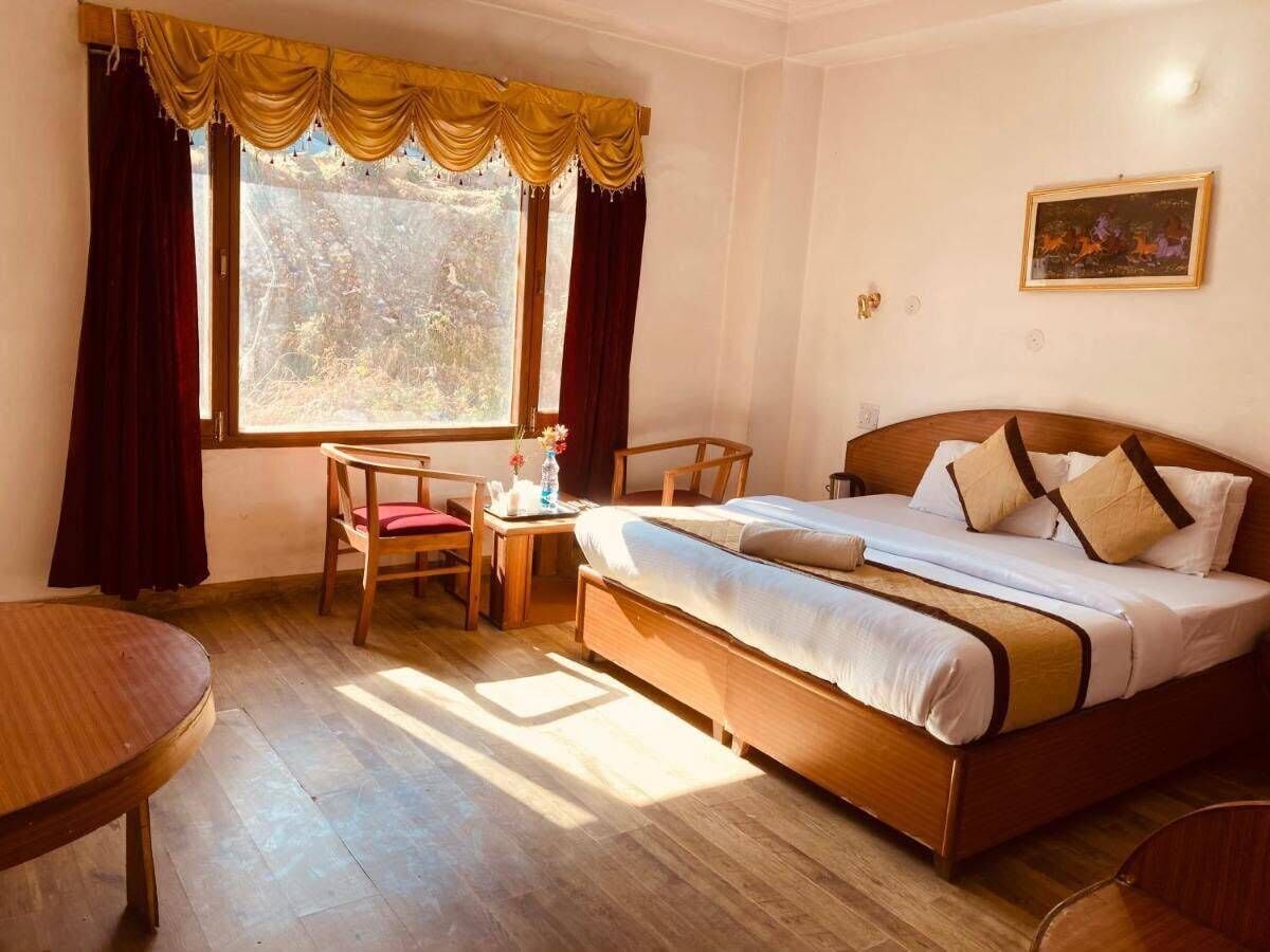 Habitación de hotel con cama, escritorio, silla y ventana con cortinas.