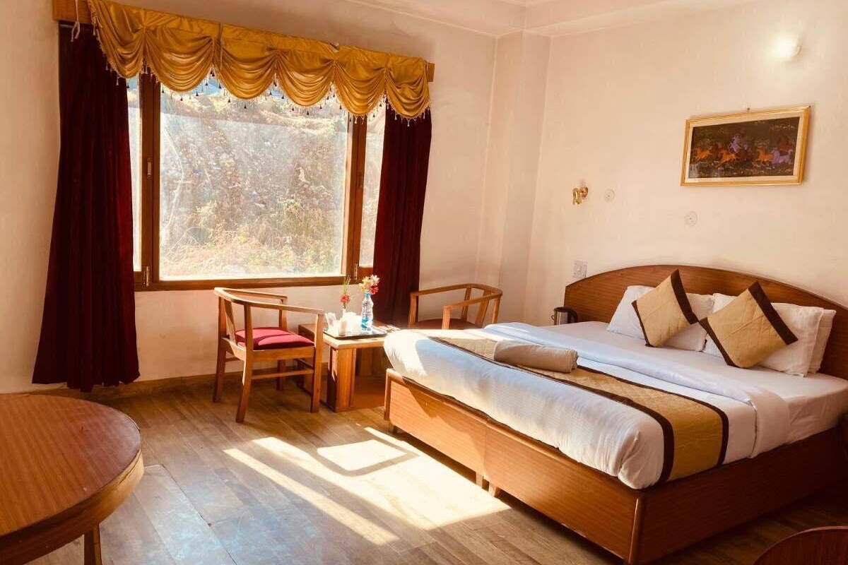 Habitación de hotel con cama, escritorio, silla y ventana con cortinas.