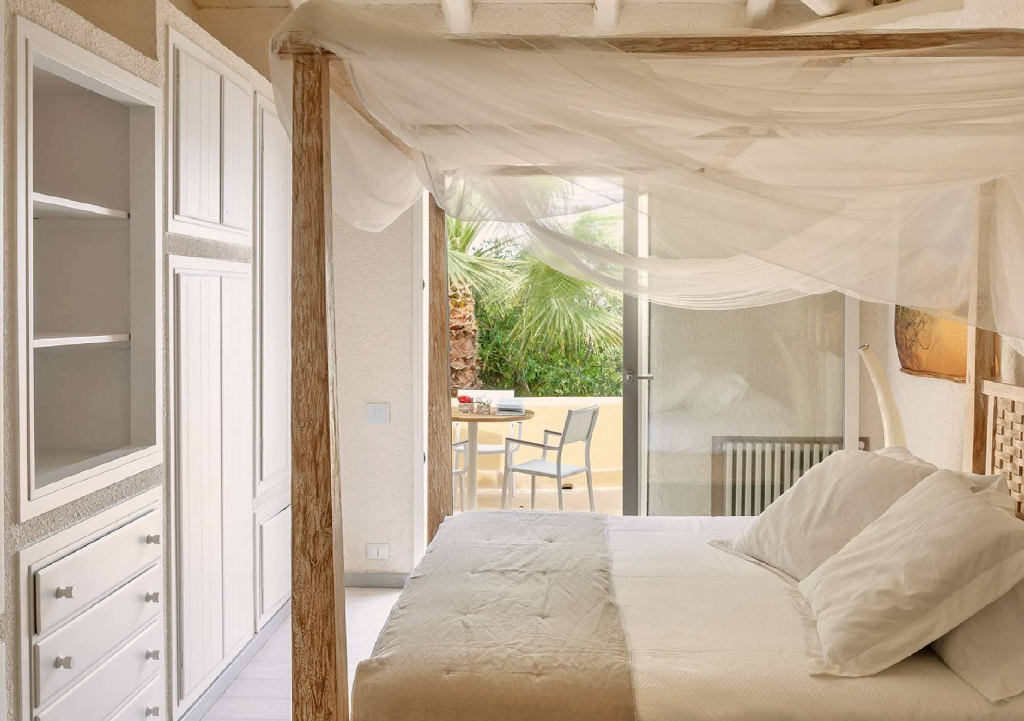 Une chambre à coucher avec un lit à baldaquin, une vue sur l’extérieur et un coin repas comprenant une table et des chaises.