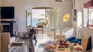 Un vaste espace de vie avec vue sur la mer, une table à manger dressée et un téléviseur fixé au mur.