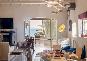 A spacious living area with a view of the sea, a dining table set with food, and a television mounted on the wall. - Elegant 7 Bedroom Villa, Pool and Panoramic Sea Views (Costa Saracena-Castelluccio)